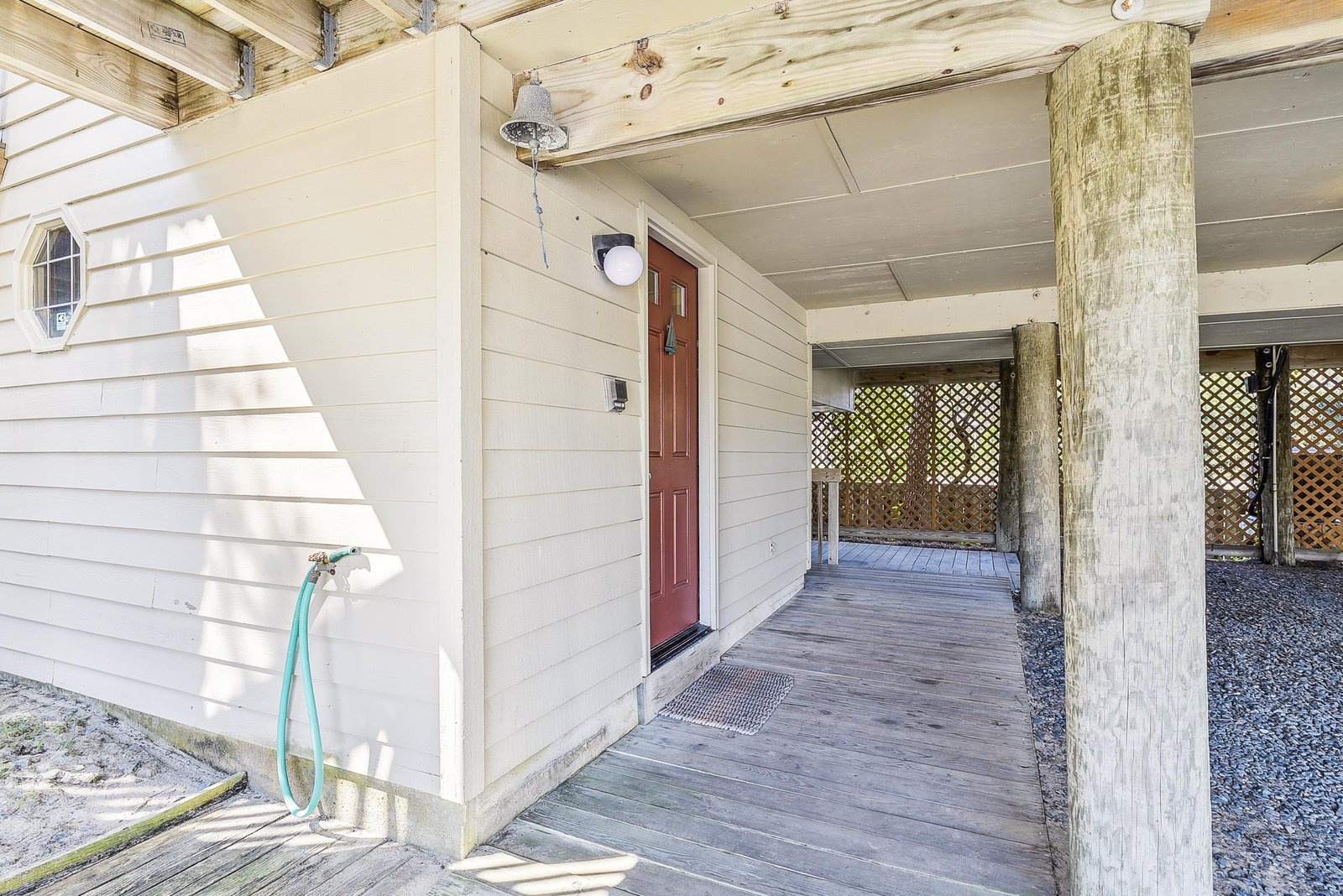 A welcoming covered walkway leads to the entrance, featuring weathered wooden pillars and a distinctive round porthole window that hints at coastal charm.