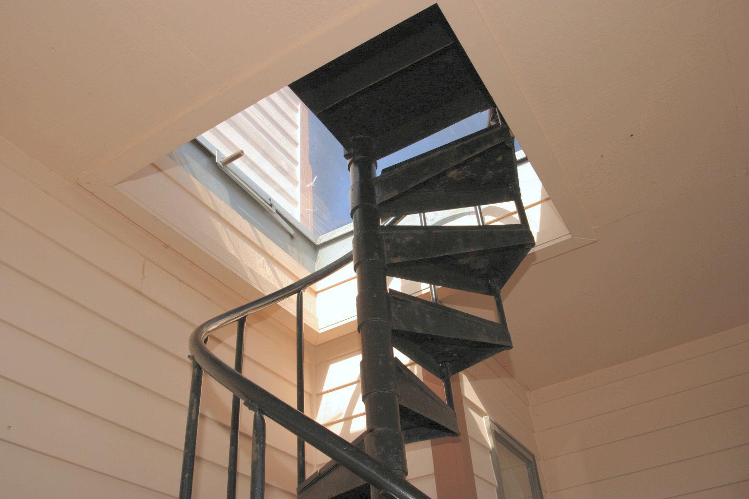 A spiral staircase winds upward toward natural light flooding through a skylight, creating an airy, open feel as you move between floors.