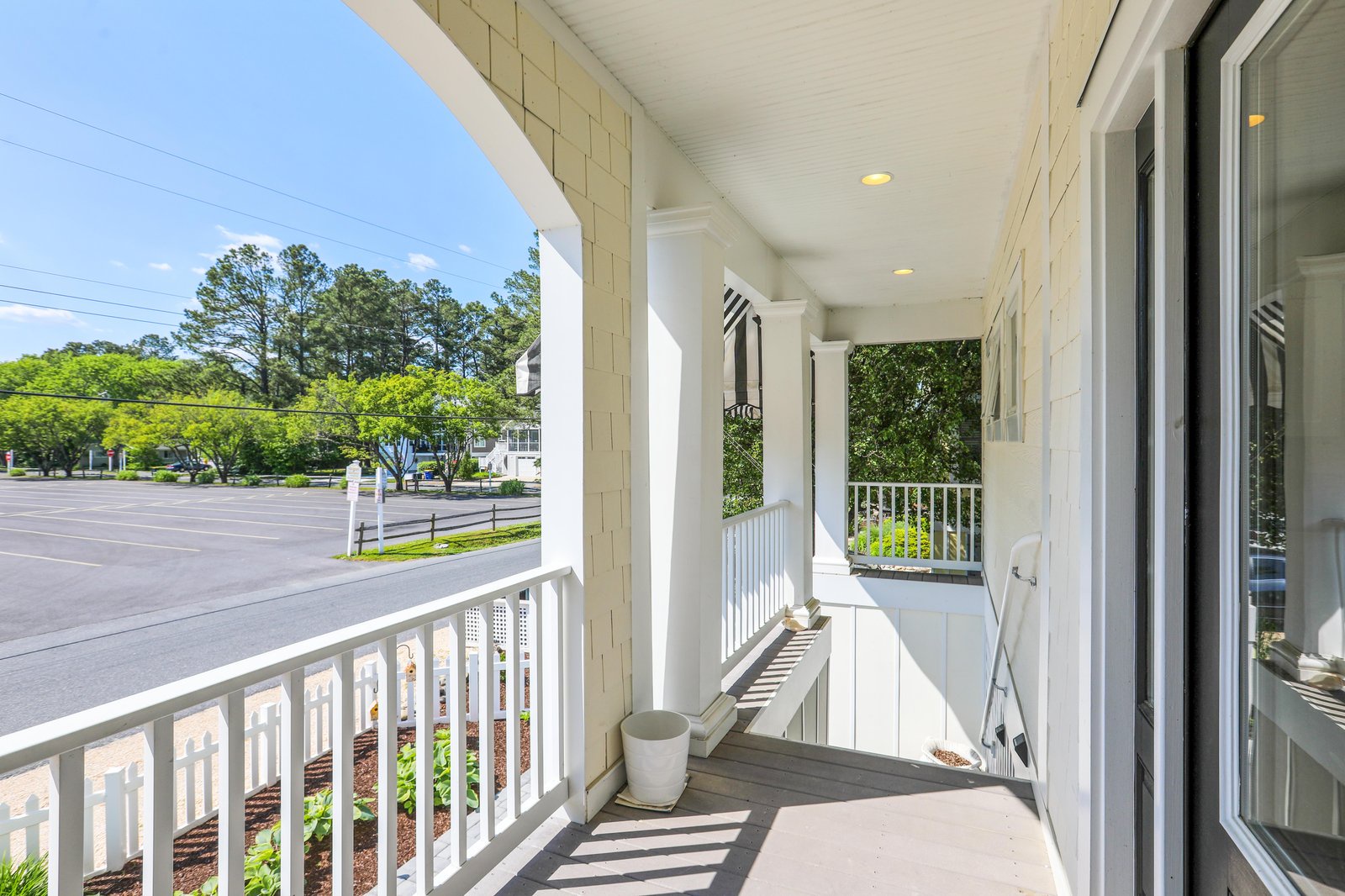 A covered balcony where you can enjoy your morning coffee while watching the neighborhood come alive, with classic white railings and peaceful tree-lined views stretching beyond the quiet street.