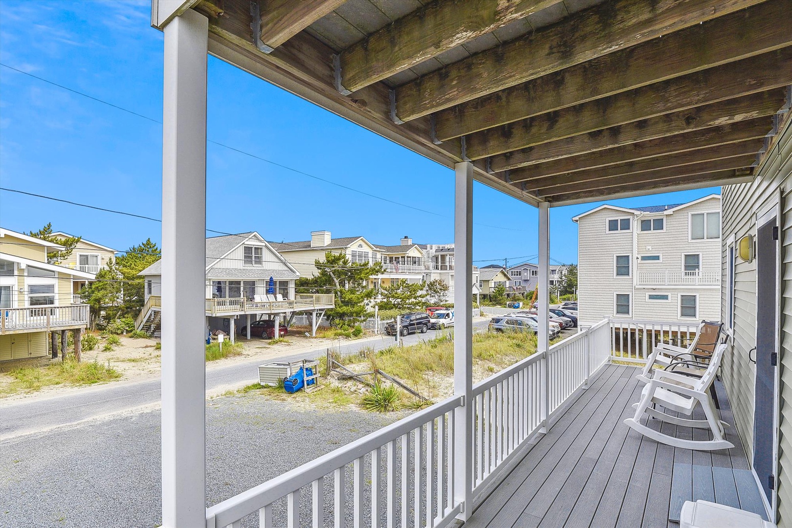 Covered porch with comfortable seating overlooking a quiet coastal neighborhood, perfect for your morning coffee or evening relaxation.