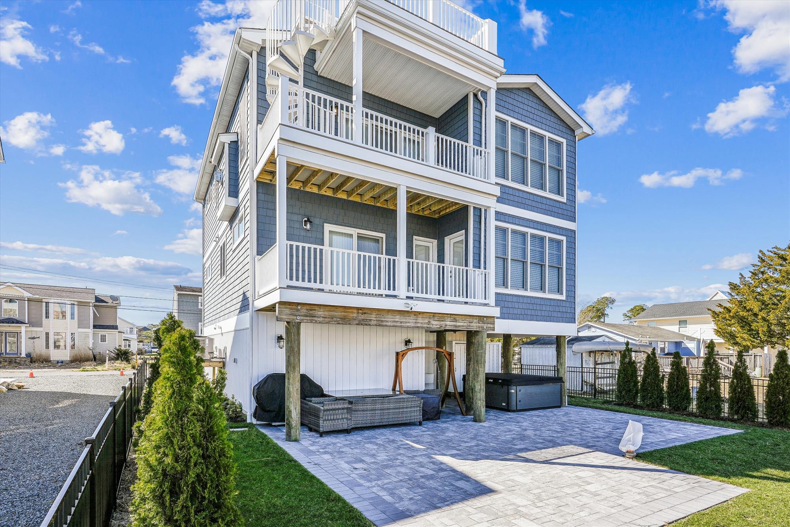A striking three-story coastal property with spacious balconies, set in a peaceful residential neighborhood. The ground-level patio features a covered seating area and hot tub, perfect for relaxation.
