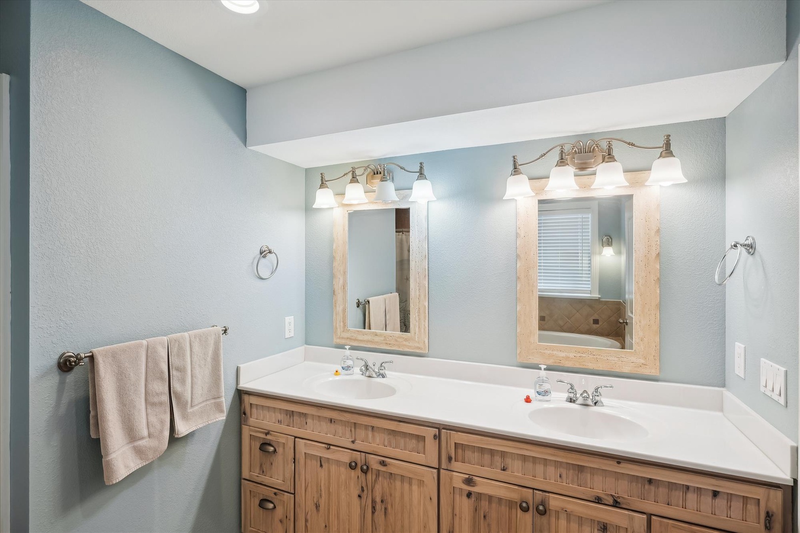 Step into your coastal-inspired bathroom with double vanity sinks, warm wood cabinetry, and soft blue walls that create a serene spa-like retreat for your morning routine.