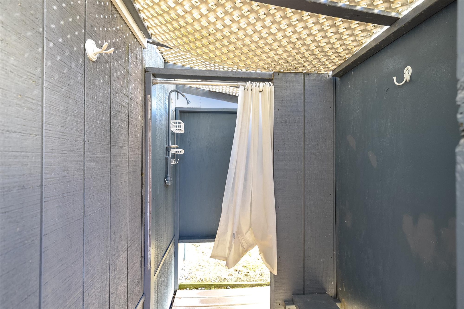 Outdoor shower surrounded by lattice roof filtering natural sunlight for refreshing rinses after beach days or poolside lounging.