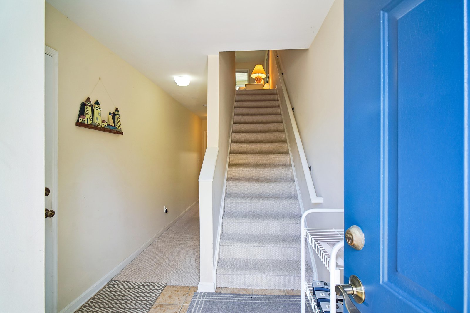 The front entrance of a vacation rental property features a bright blue door opening into a welcoming foyer with carpeted stairs leading to the upper level.