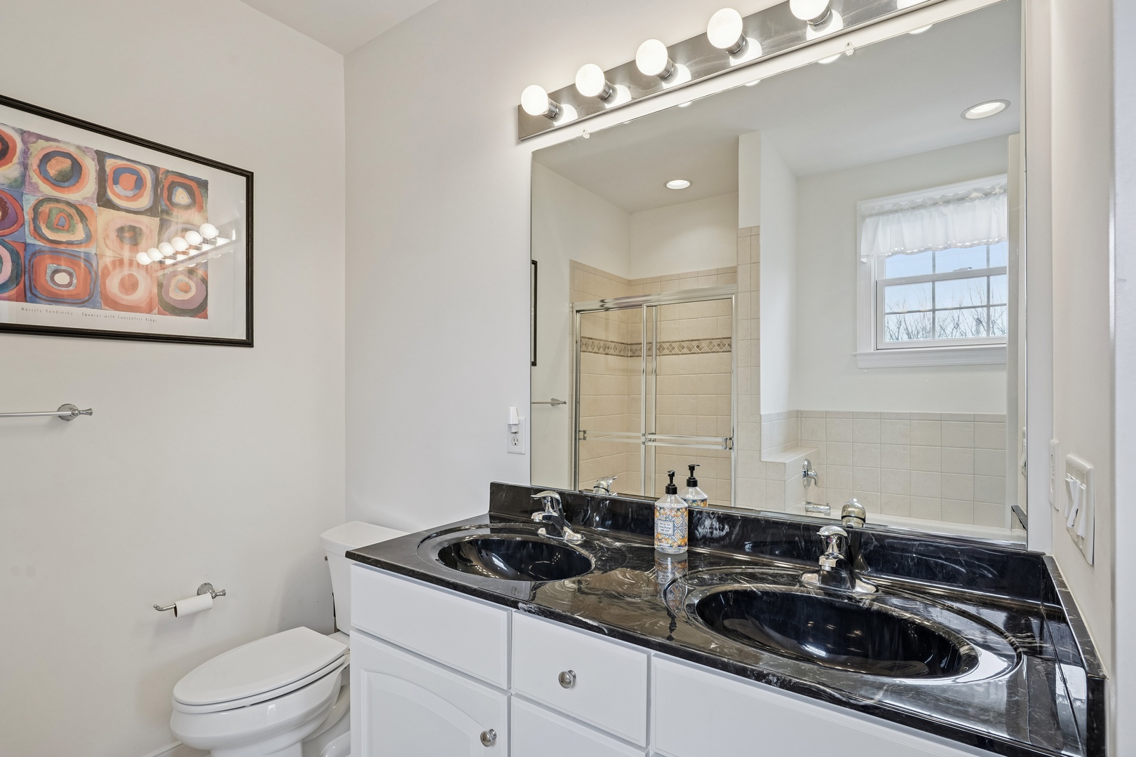 Step into your elegant private bathroom featuring dual vanity sinks with gleaming black marble countertops and Hollywood-style vanity lighting.