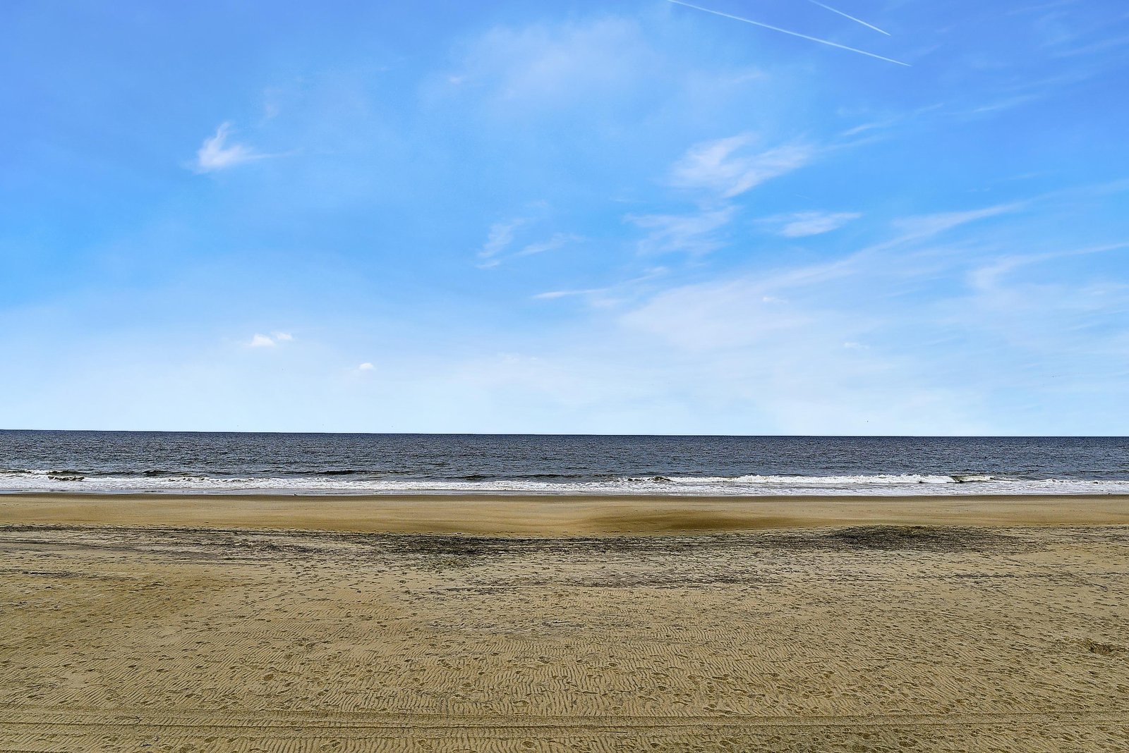 Wide open sandy beach meets the ocean under a clear blue sky, offering a peaceful escape just moments from the property.