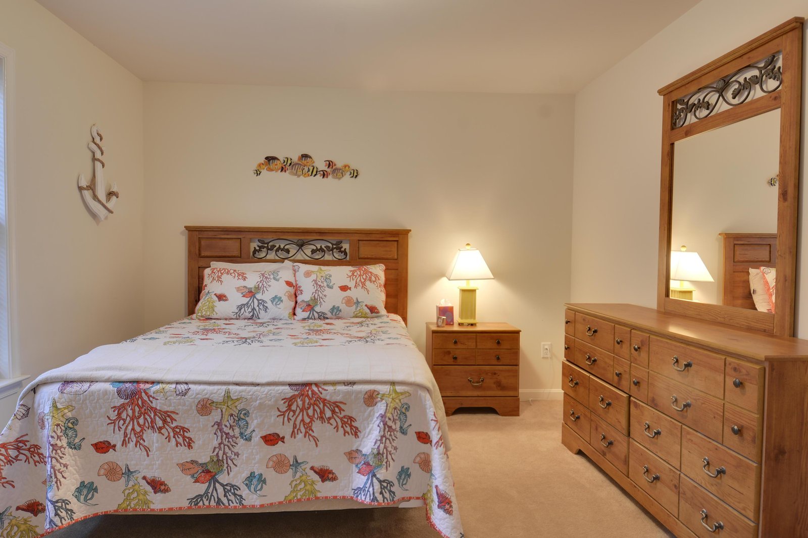 Your cozy bedroom awaits with warm wood accents, a plush bed dressed in cheerful coral and sea life linens, and a peaceful coastal ambiance to help you unwind.