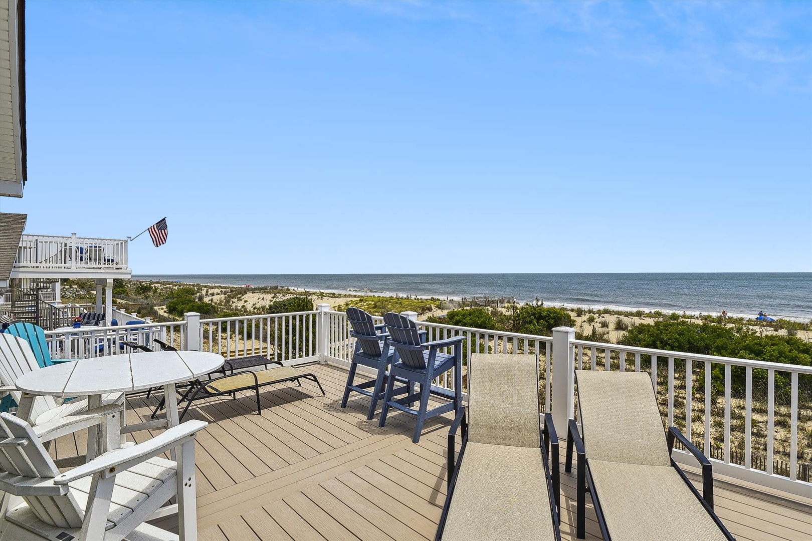 Spacious beachfront deck with Adirondack chairs, dining table, and sweeping ocean views—perfect for morning coffee or watching gentle waves roll in.