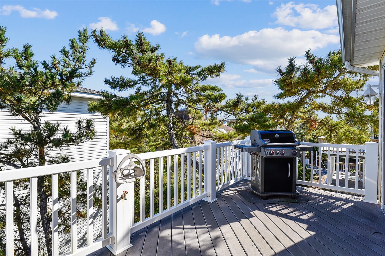This private deck features a gas grill surrounded by mature pine trees, offering a peaceful outdoor space for al fresco dining and coastal relaxation in the neighborhood's natural setting.