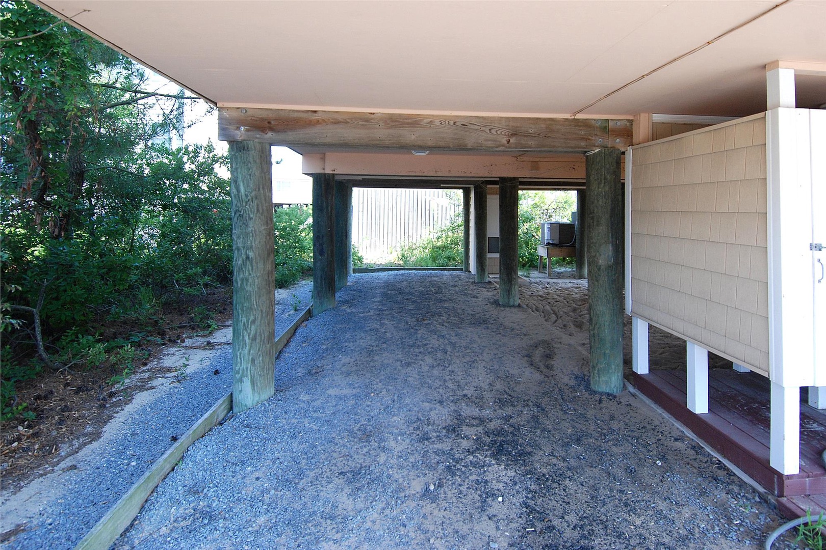 The property features convenient covered parking beneath the main structure, with rustic wooden beams framing your protected parking area surrounded by natural coastal greenery.