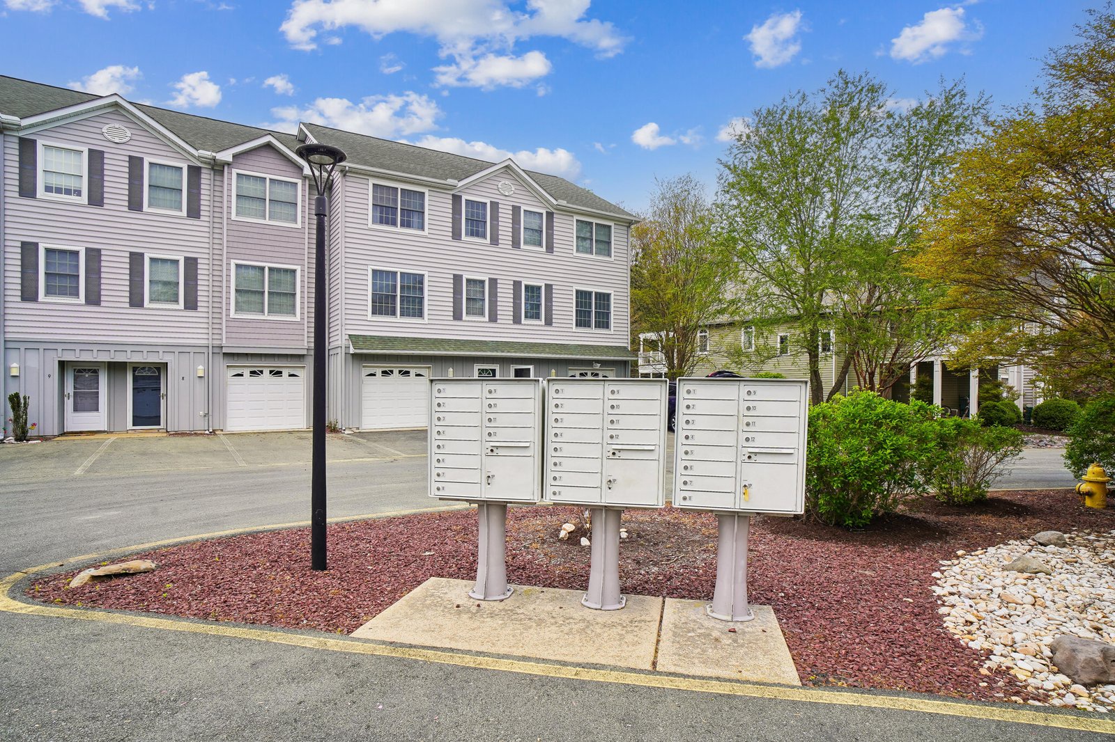 Residential building exterior featuring multiple units with garage access, set in a landscaped community with mature trees and maintained grounds.