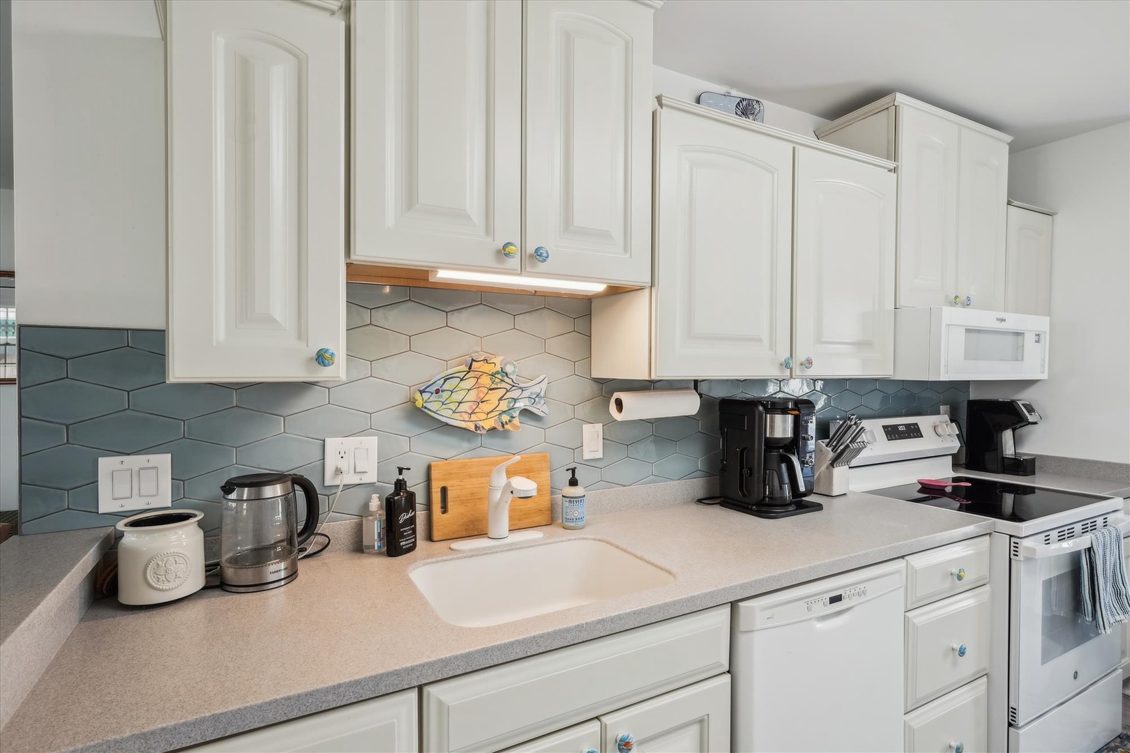 Step into your fully equipped kitchen, where coastal charm meets modern convenience. Bright white cabinetry, stylish teal backsplash, and stainless appliances invite you to prepare memorable meals in comfort.