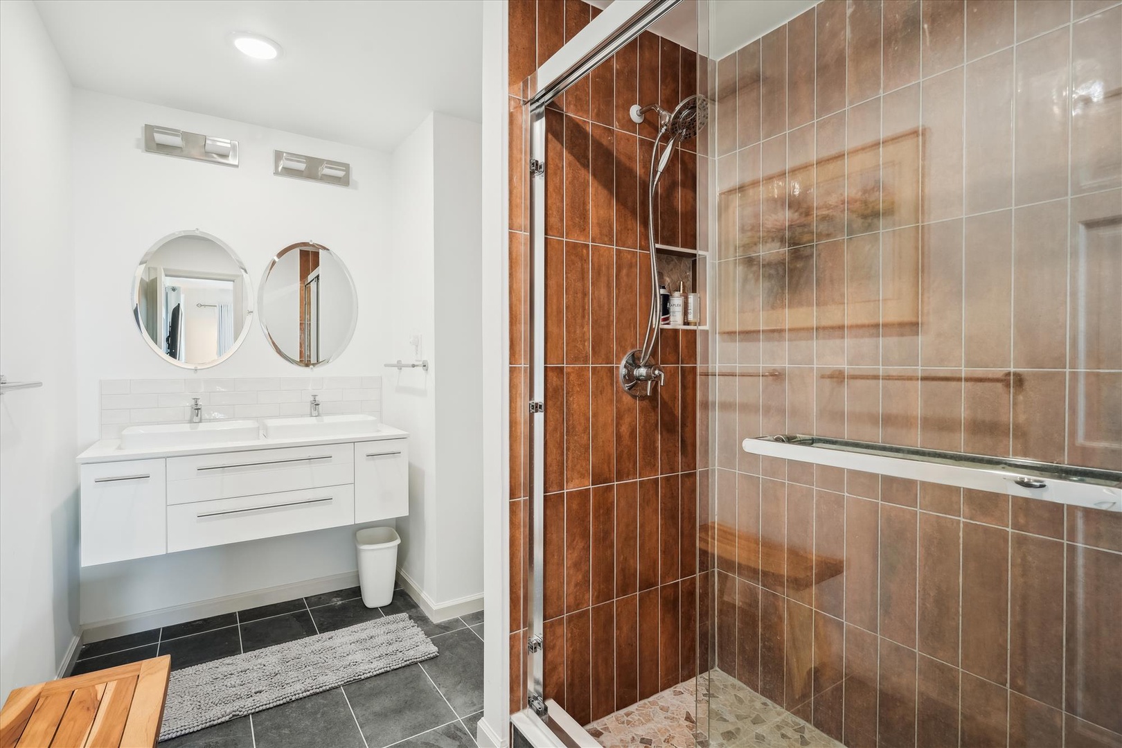Refresh and unwind in your modern bathroom featuring dual vanities, warm wood-tone tiles, and a spacious glass-enclosed shower designed for ultimate relaxation.