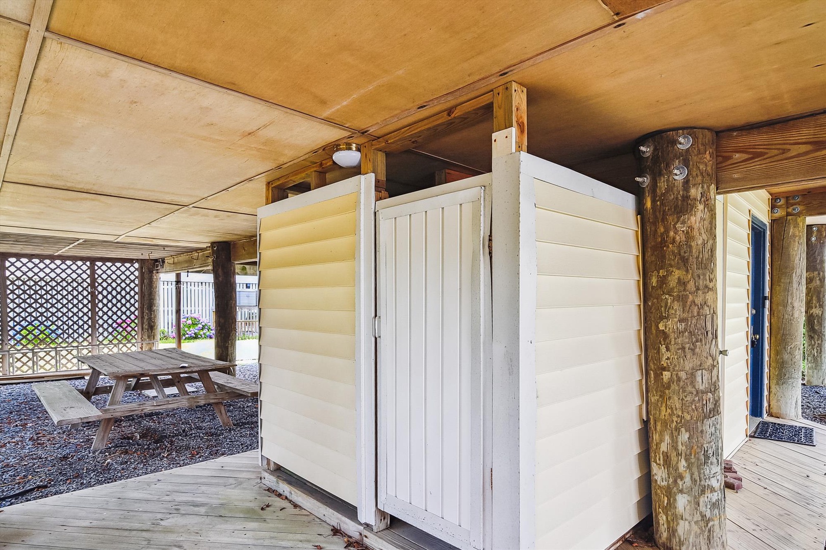 Covered outdoor area with rustic wood beams, picnic table, and convenient shower enclosure for refreshing after your beach or pool time.