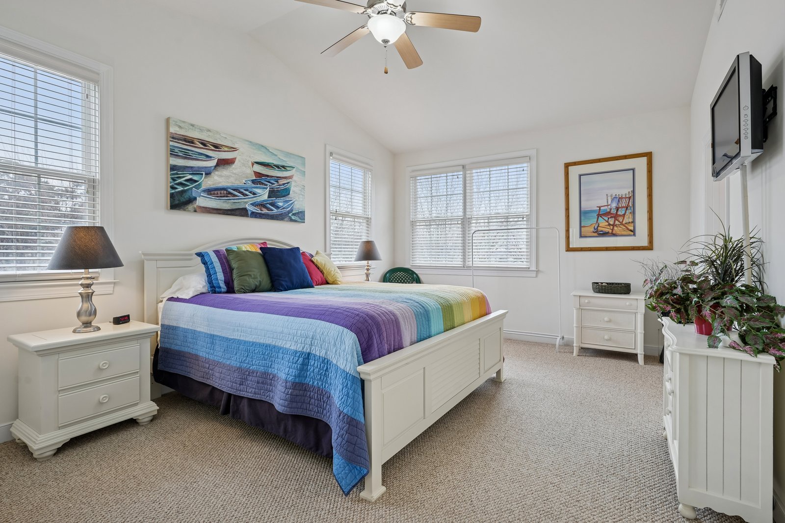 Drift off in your bright coastal bedroom with vibrant bedding, nautical artwork, and a ceiling fan for perfect comfort.