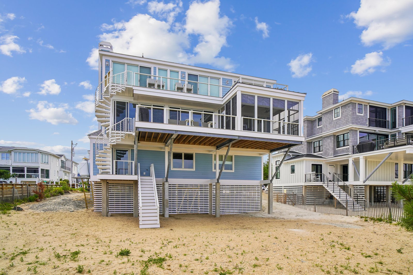 This elevated beachfront property features expansive wraparound balconies, multiple levels of outdoor living space, and direct access to the sand, with neighboring coastal homes completing the seaside setting.