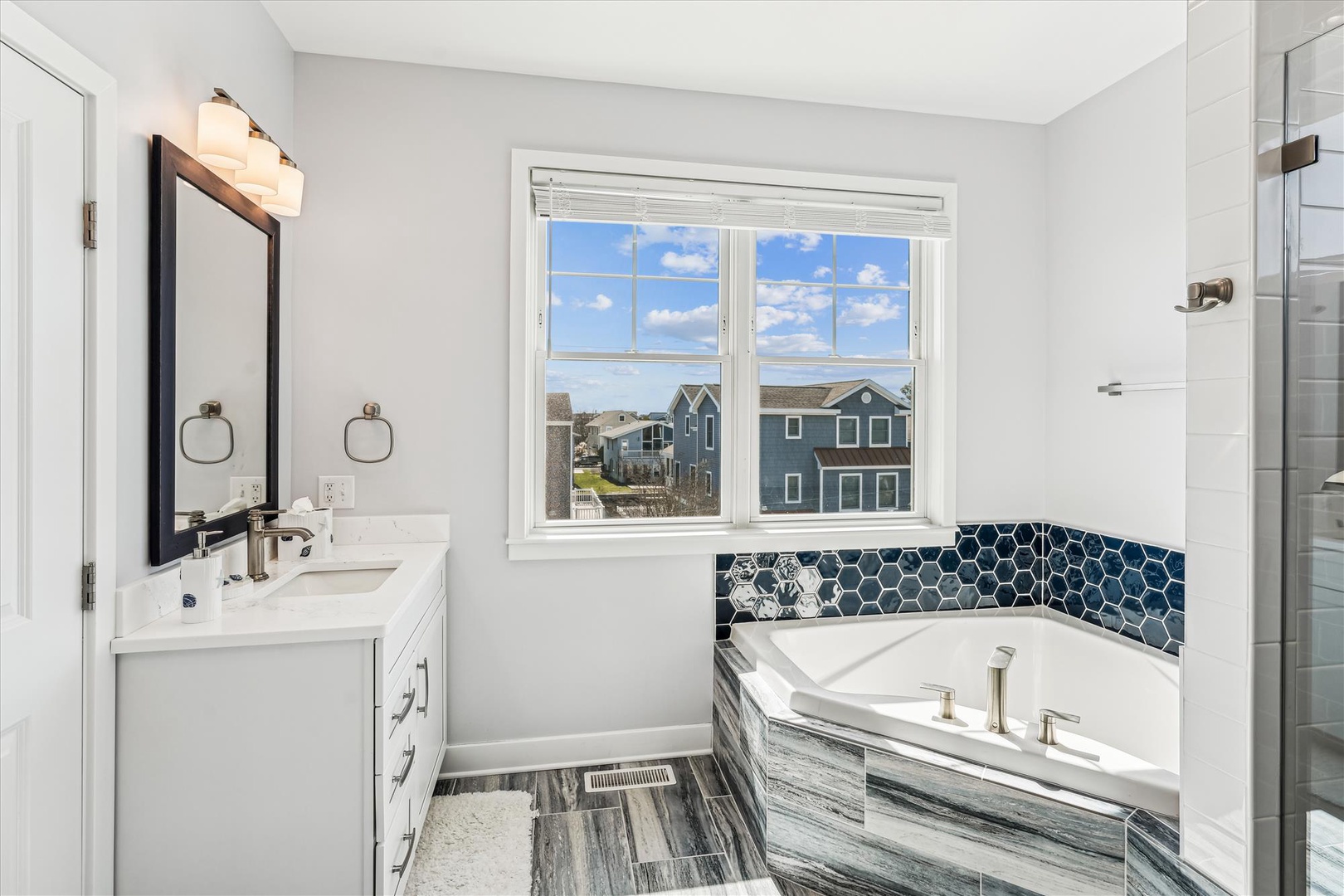 Soak in style with your own luxurious bathtub featuring stunning blue hexagonal tiles and peaceful neighborhood views through the bright window.