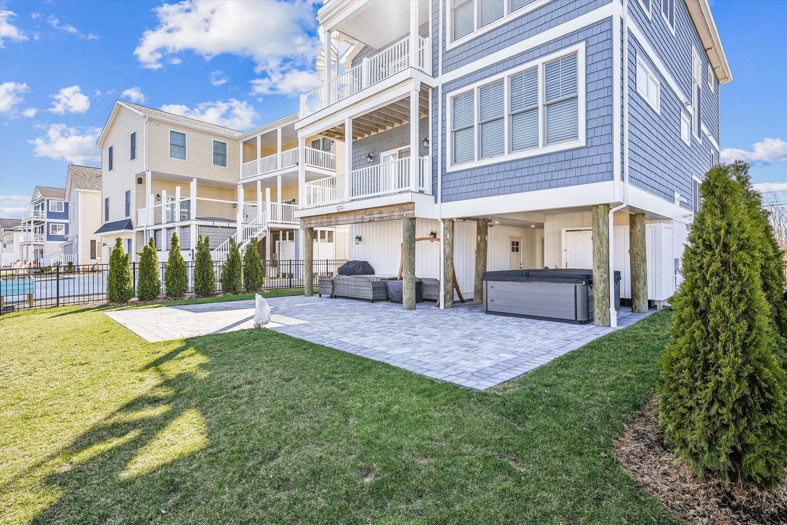 Coastal waterfront property features expansive multi-level outdoor living with balconies, heated pool, private patio with hot tub, and manicured lawn bordered by evergreens.