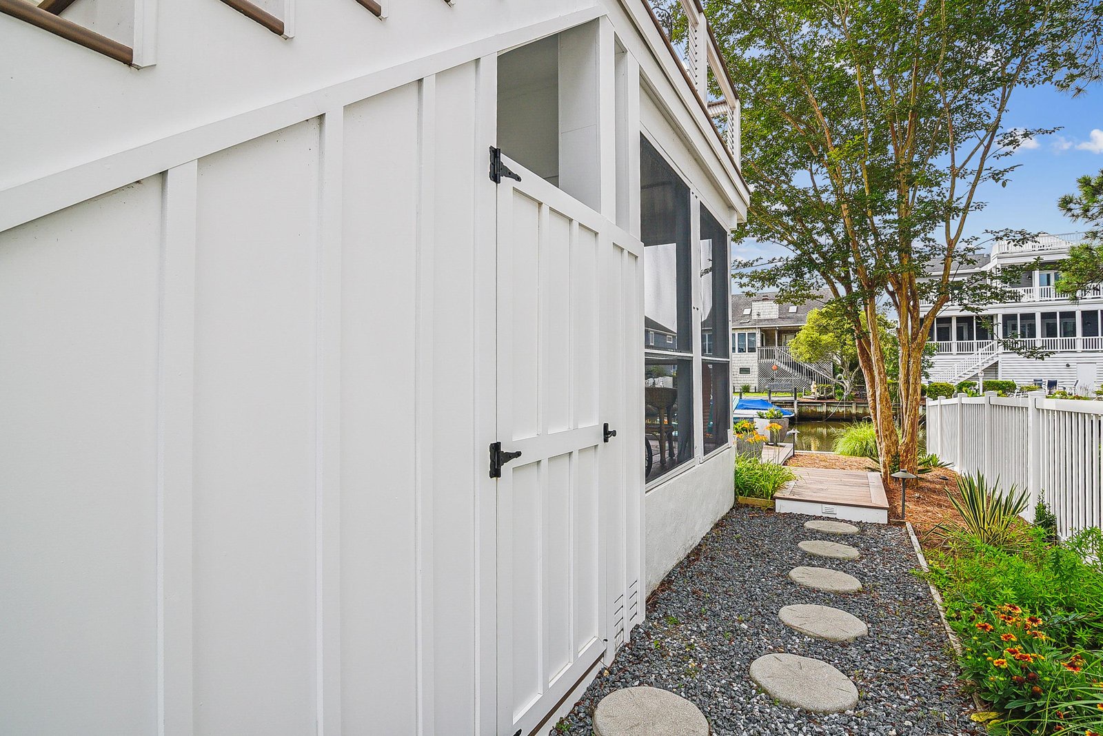 A charming outdoor path leads you along the side of the property, where coastal landscaping and stepping stones guide your way through a peaceful waterfront setting.