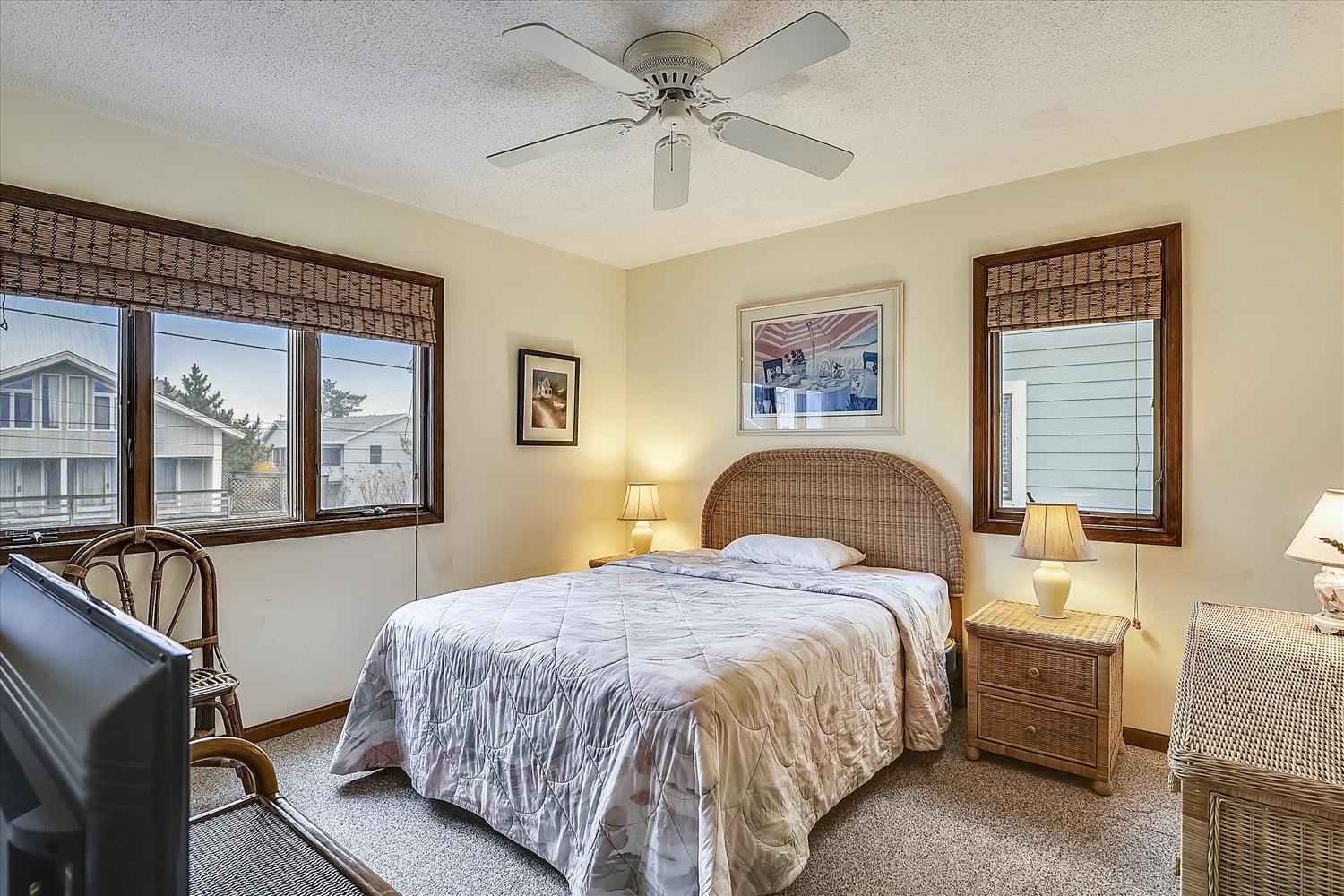 Your bright and cozy bedroom features a comfortable bed with coastal charm, bamboo shades filtering natural light, and a ceiling fan to keep you cool all night.