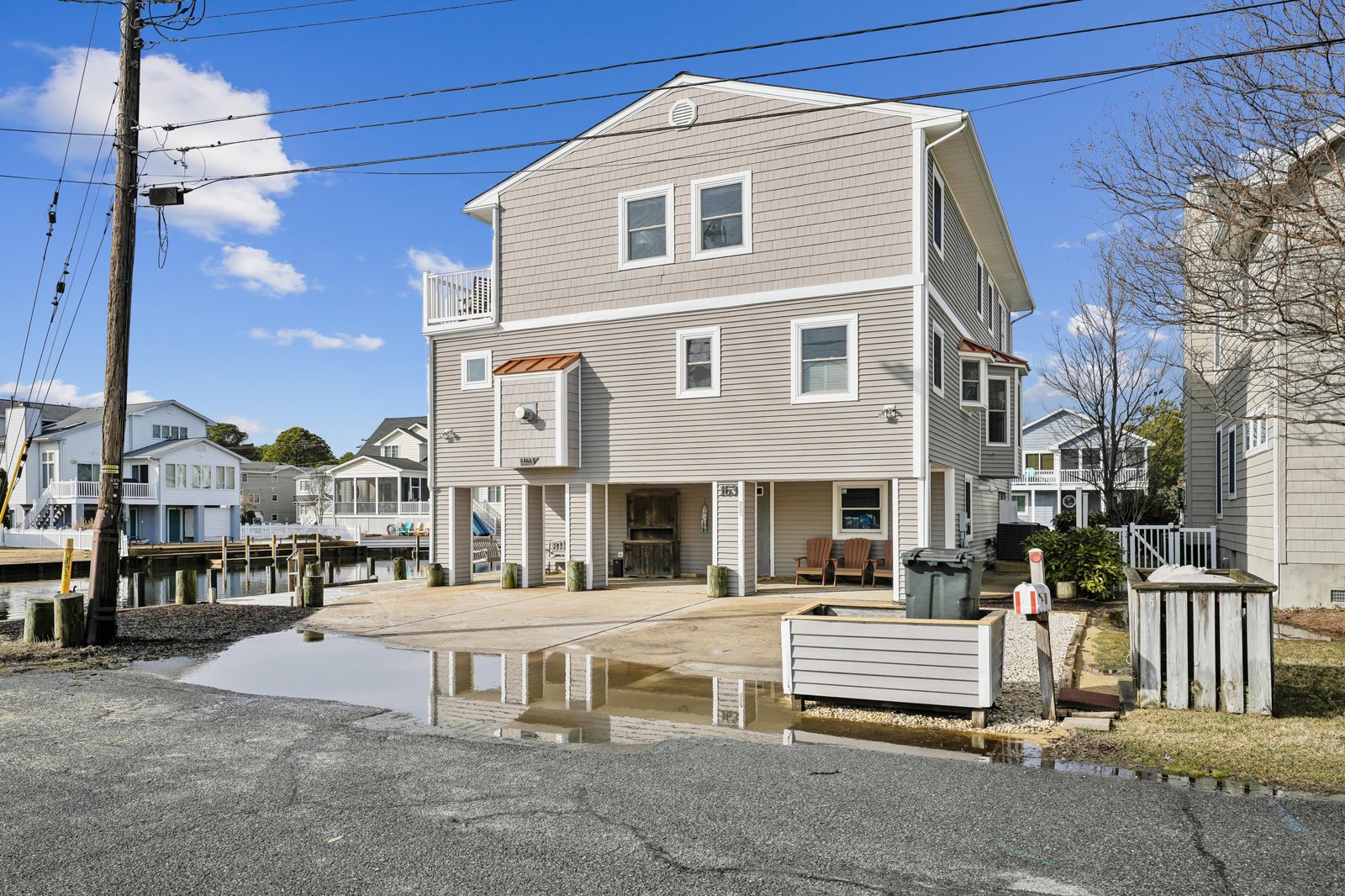 Waterfront property with elevated two-story design on a quiet residential street, featuring covered ground-level parking and neighboring homes along the canal.
