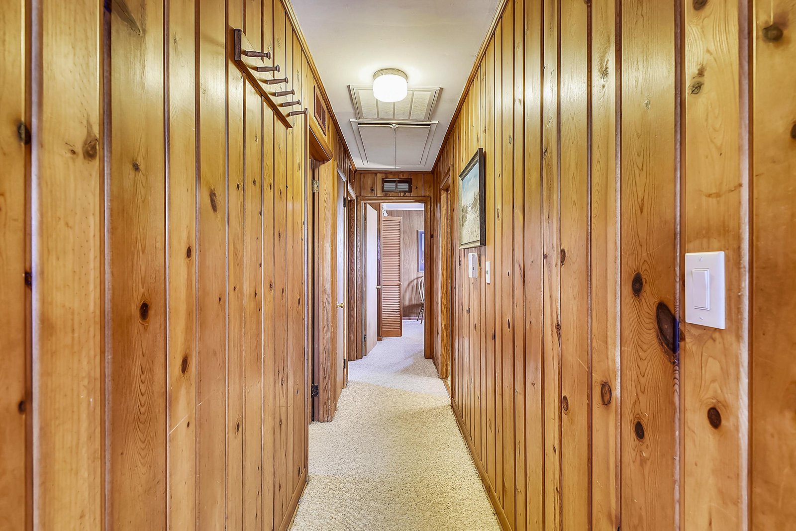 Warm knotty pine walls line your hallway, adding rustic charm and natural character to your stay. Soft carpet underfoot and abundant overhead lighting create a welcoming path to your private spaces.