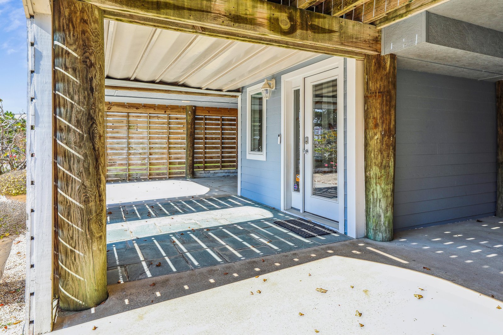 A covered entry welcomes you with rustic charm and coastal ease. Natural wood posts and slatted screens filter soft light and sea breezes, setting a relaxed tone the moment you arrive.