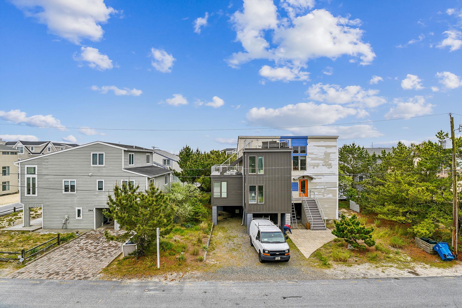 Modern coastal architecture nestled in a quiet beach community, surrounded by natural dunes and greenery under bright blue skies.