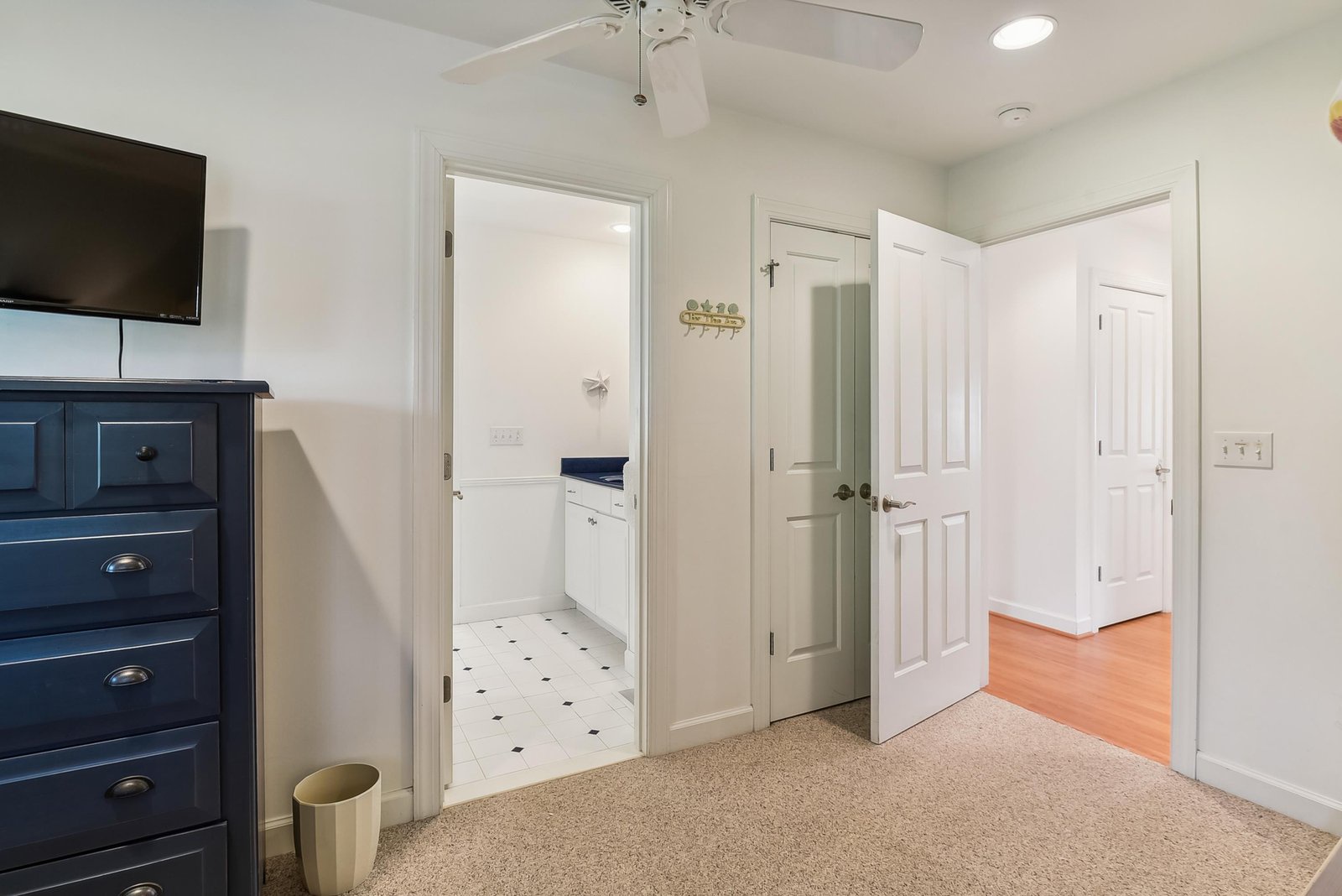 A bright bedroom space opens to an ensuite bath, with ceiling fan, wall-mounted TV, and a wardrobe tucked conveniently beside the door—everything you need for a restful stay.