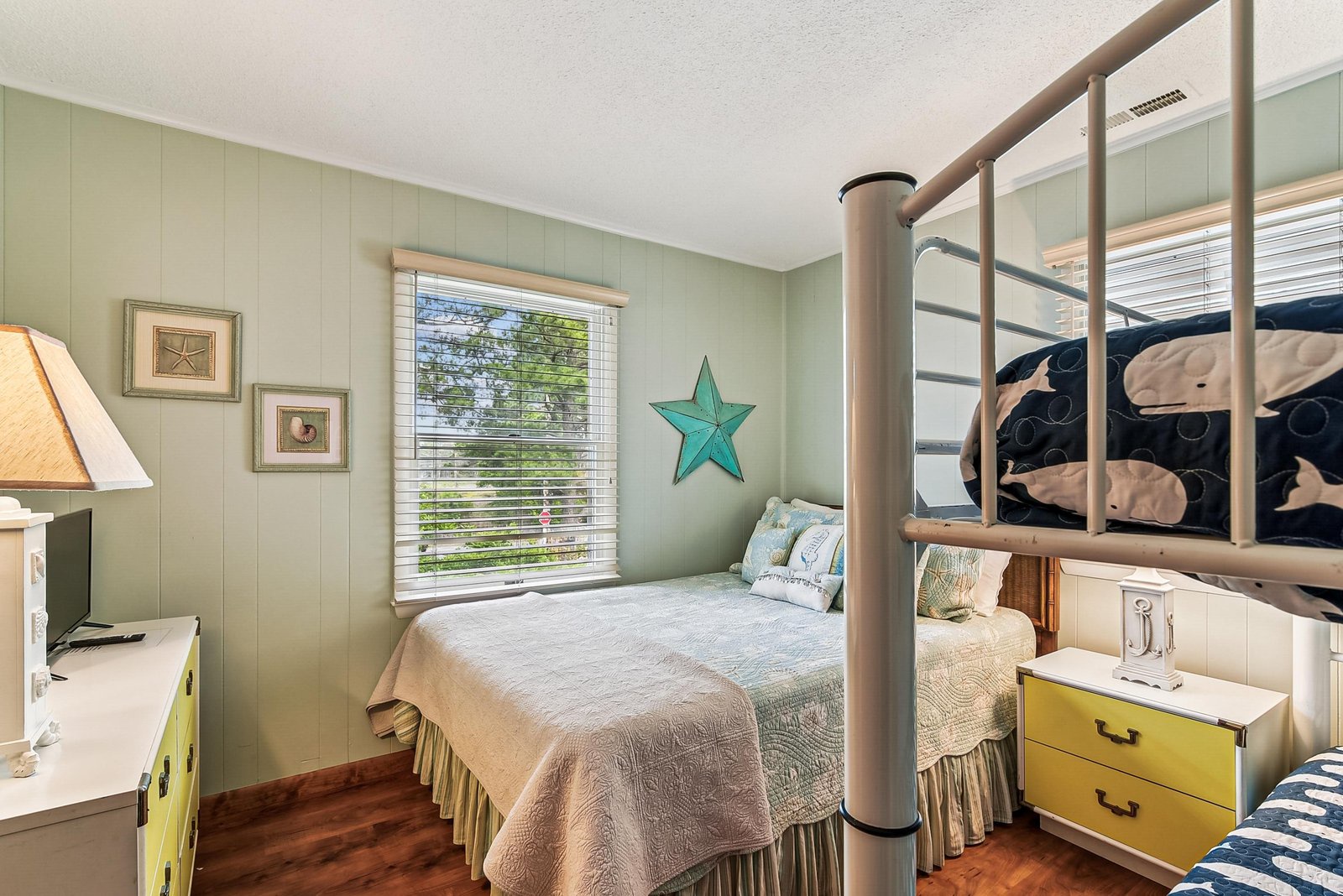 Sink into coastal comfort in your serene bedroom with soothing sage walls, charming nautical touches, and soft natural light filtering through the blinds. Perfect for peaceful nights after beachside days.