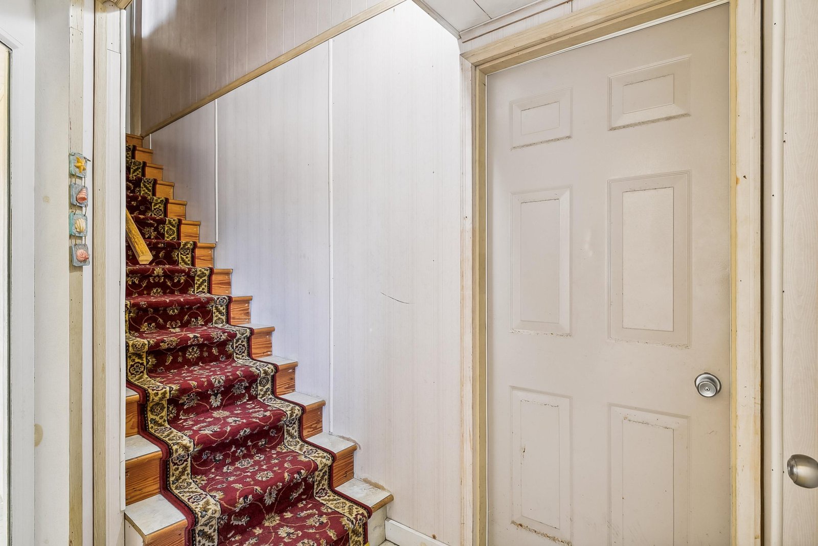 A charming staircase with warm wood steps and decorative carpet runner leads to your private upper-level space, tucked neatly behind clever under-stair storage.