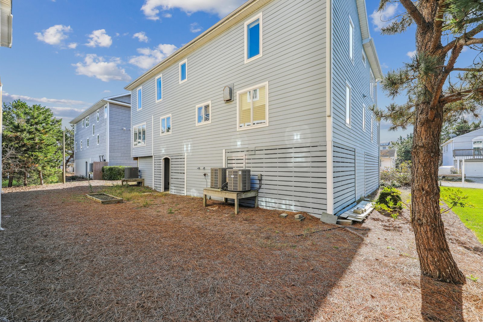 The property stands among a quiet neighborhood setting, with mature trees and open space visible nearby. The blue sky and natural surroundings frame this vacation rental.