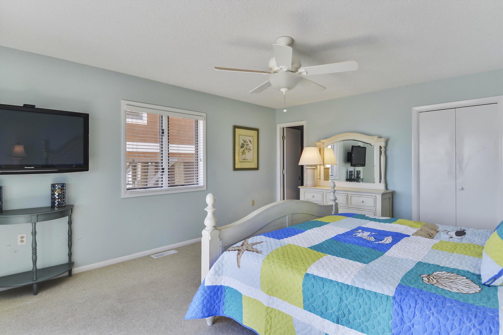 Your peaceful bedroom retreat features a breezy ceiling fan, soft coastal tones, and a cheerful quilt inviting you to unwind after a day of adventure.