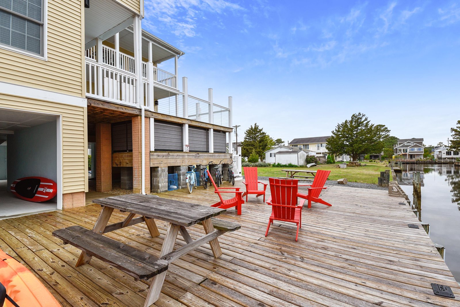 The waterfront deck extends over the canal, offering bright red Adirondack chairs and a picnic table where you can soak in calm water views and coastal sunshine. Kayaks and bikes are ready for your next adventure.