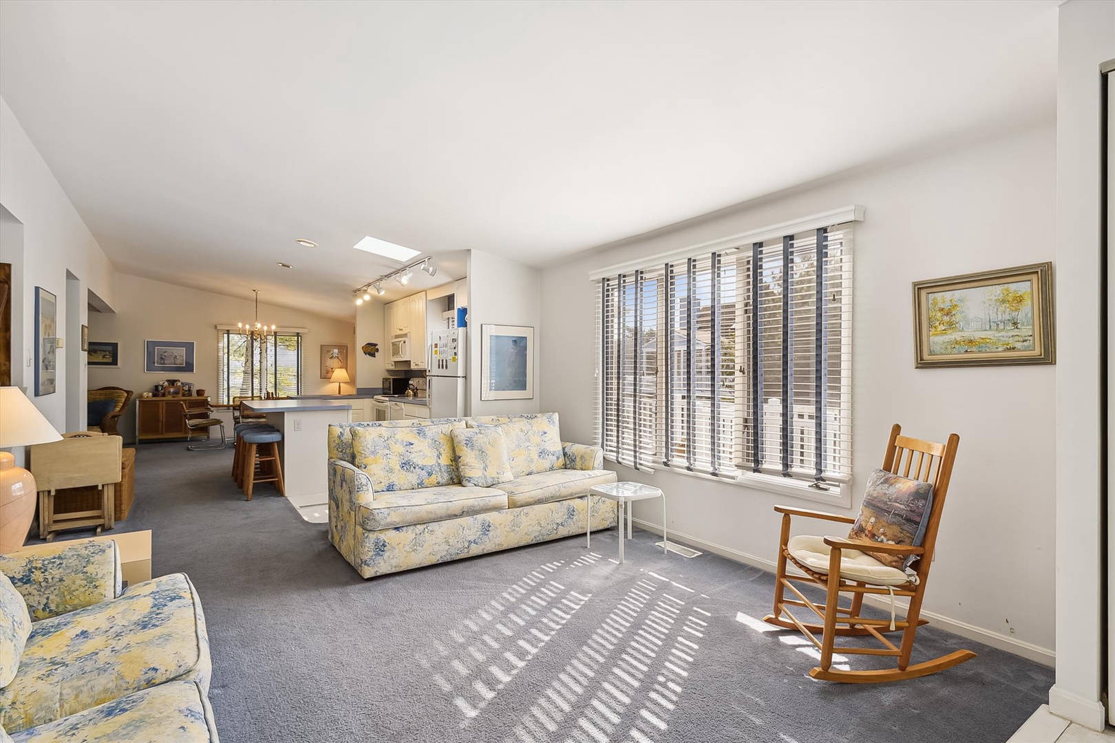 Sunlight streams through plantation blinds into your spacious open-plan living area, where a cozy floral sofa and classic rocking chair invite you to unwind in comfort.