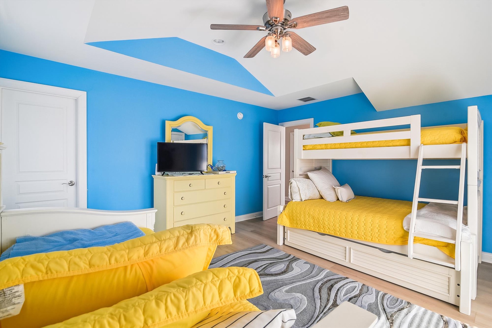 Your family will love this cheerful bedroom with bright blue walls, a white bunk bed with sunny yellow linens, twin beds, and a ceiling fan to keep everyone comfortable.