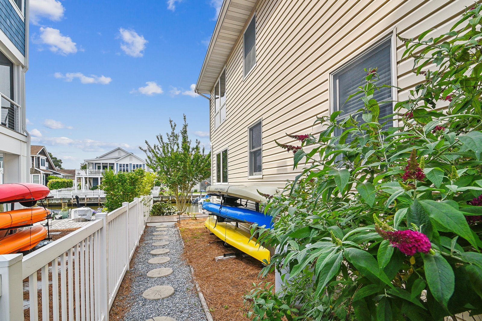 The path beside the property leads past kayak storage and a flowering garden—perfect for easy waterside access during your beach getaway.