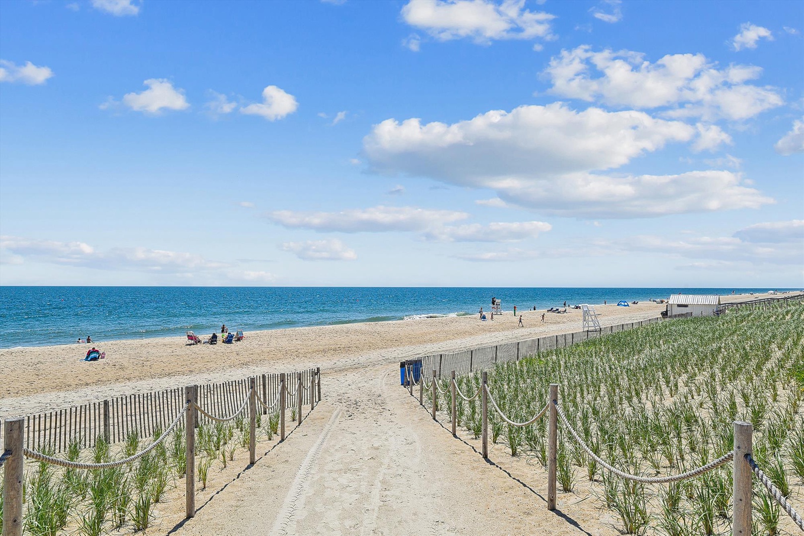 A pristine beach with soft sand and clear blue waters stretches along the coast, offering a peaceful escape with protected dunes and a scenic pathway leading to the shore.