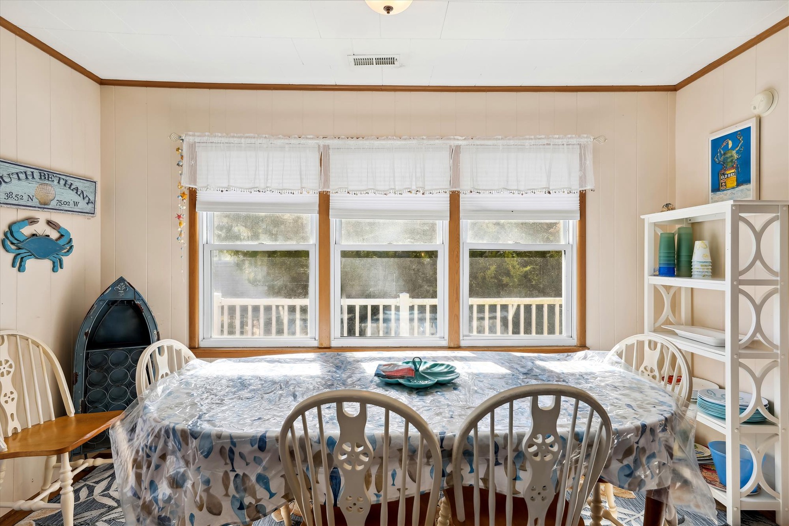 Gather around this cheerful dining space where coastal charm meets home comfort. Natural light pours through triple windows framing your outdoor deck views, while nautical touches add character to every meal.