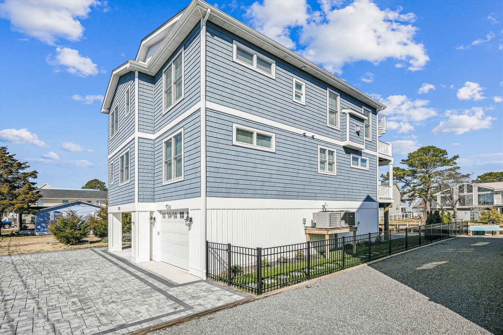 A modern beach house with sleek blue siding and contemporary architecture, situated in a coastal neighborhood with nearby waterfront access and ample outdoor parking.
