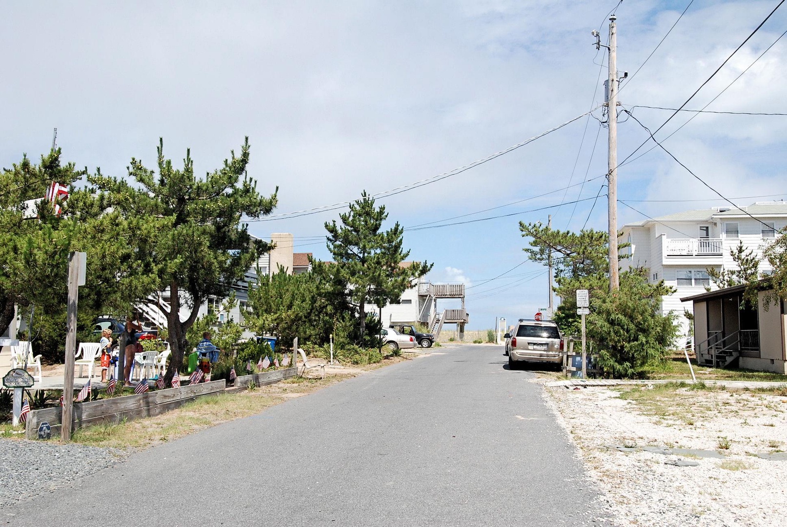 A quiet coastal street lined with trees and vacation homes leads toward the beach, offering peaceful neighborhood charm and seaside access.