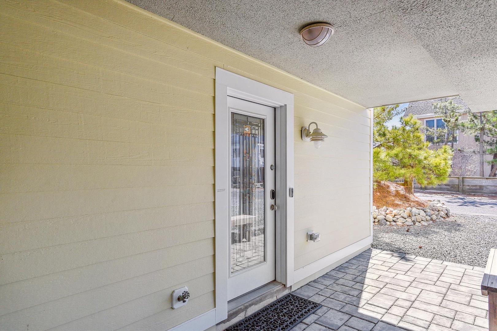 Covered entrance features decorative glass door and paver walkway, leading to a quiet residential setting with mature landscaping.