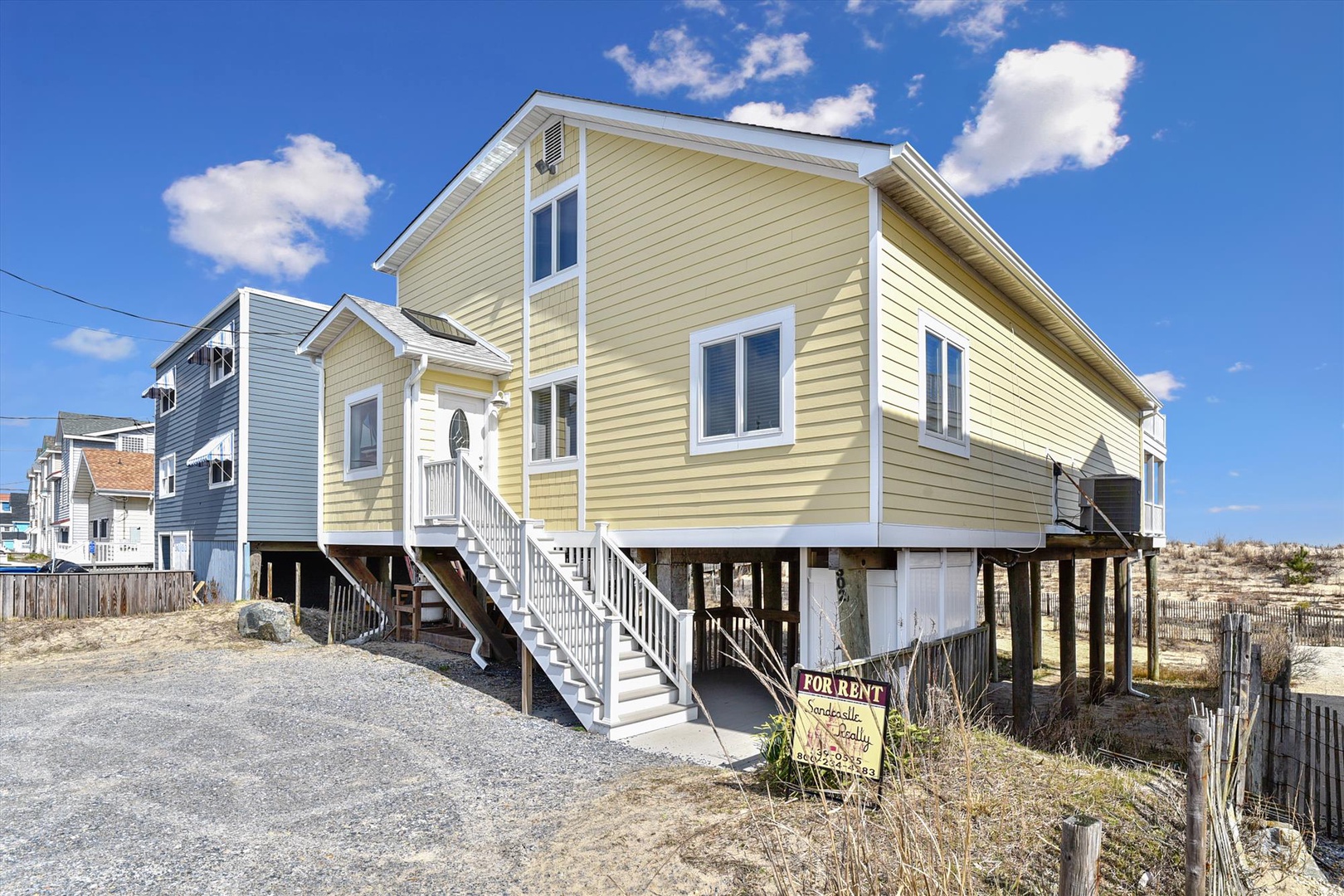 Elevated beach house with direct access to sandy shores, featuring charming yellow siding and spacious windows. A coastal retreat designed for seaside living.