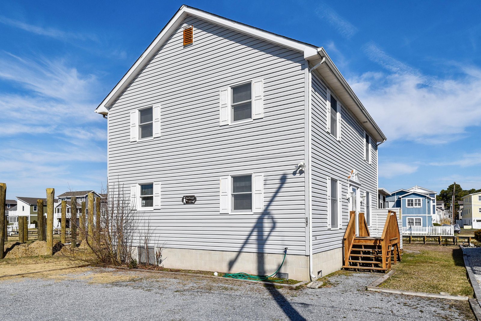 A bright coastal retreat with fresh exterior siding and a welcoming wooden deck. The clear blue skies and surrounding neighborhood set the scene for a relaxing getaway.