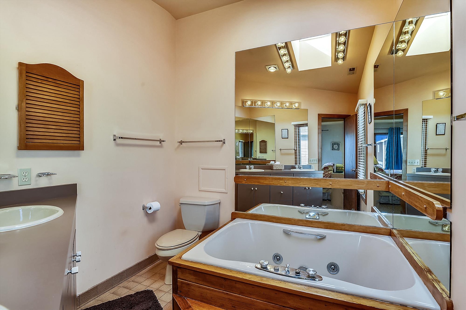Unwind in your spacious private bathroom featuring a relaxing jetted tub, double vanity, and plenty of natural light streaming through the skylight above.