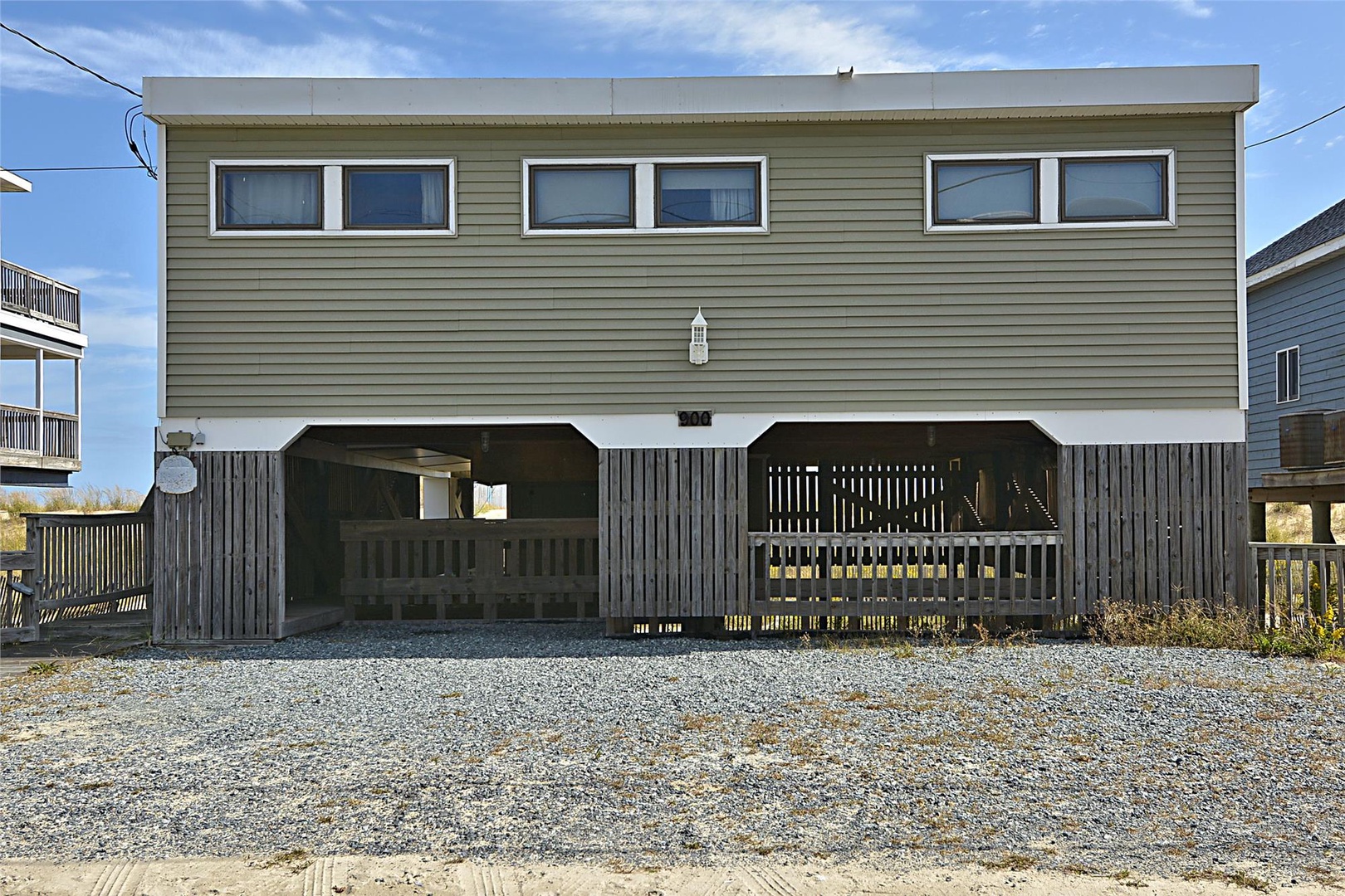 Modern beach house with covered ground-level parking, elevated living space, and multiple windows framing coastal surroundings.