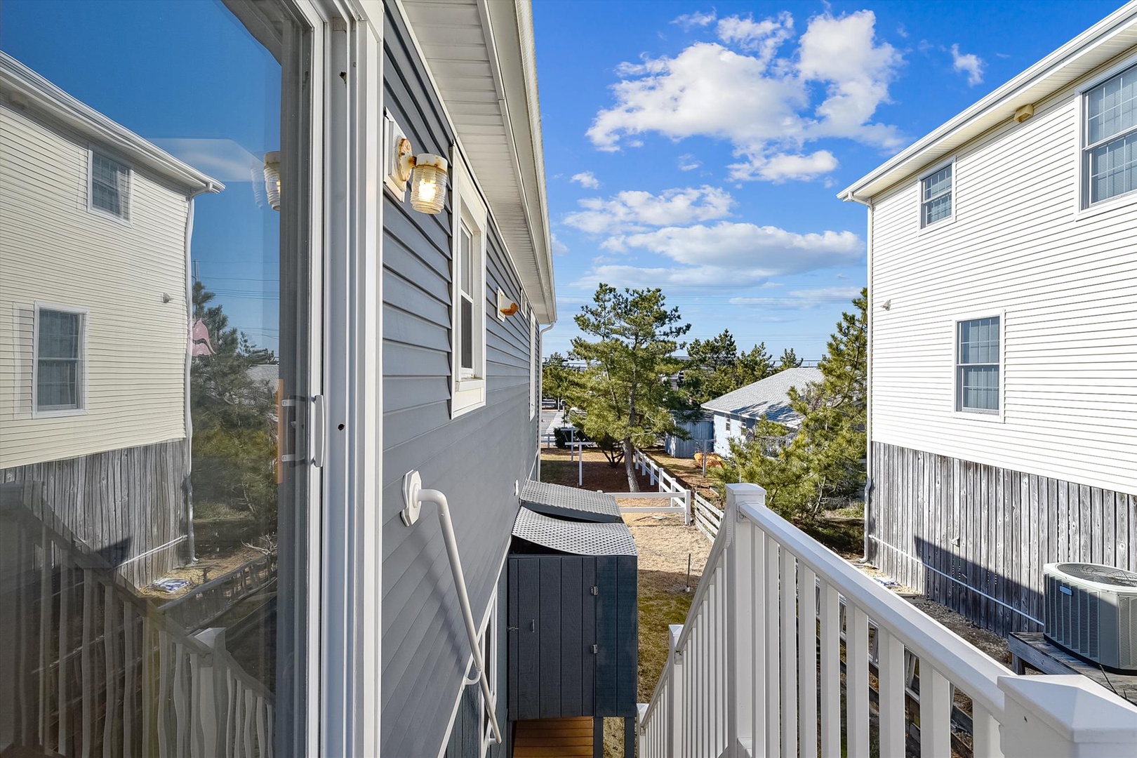 A small balcony framing neighboring beach cottages, coastal pines, and open blue skies—a peaceful backdrop to your seaside getaway.