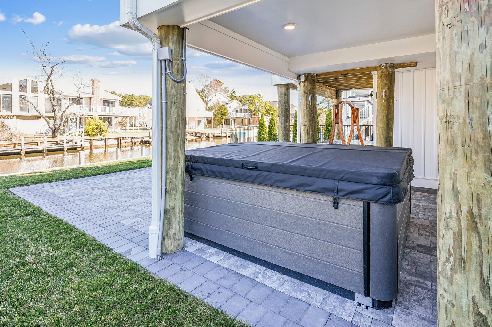 Soak under your private covered patio, where a hot tub awaits just steps from tranquil waterfront views and green lawn—pure relaxation.