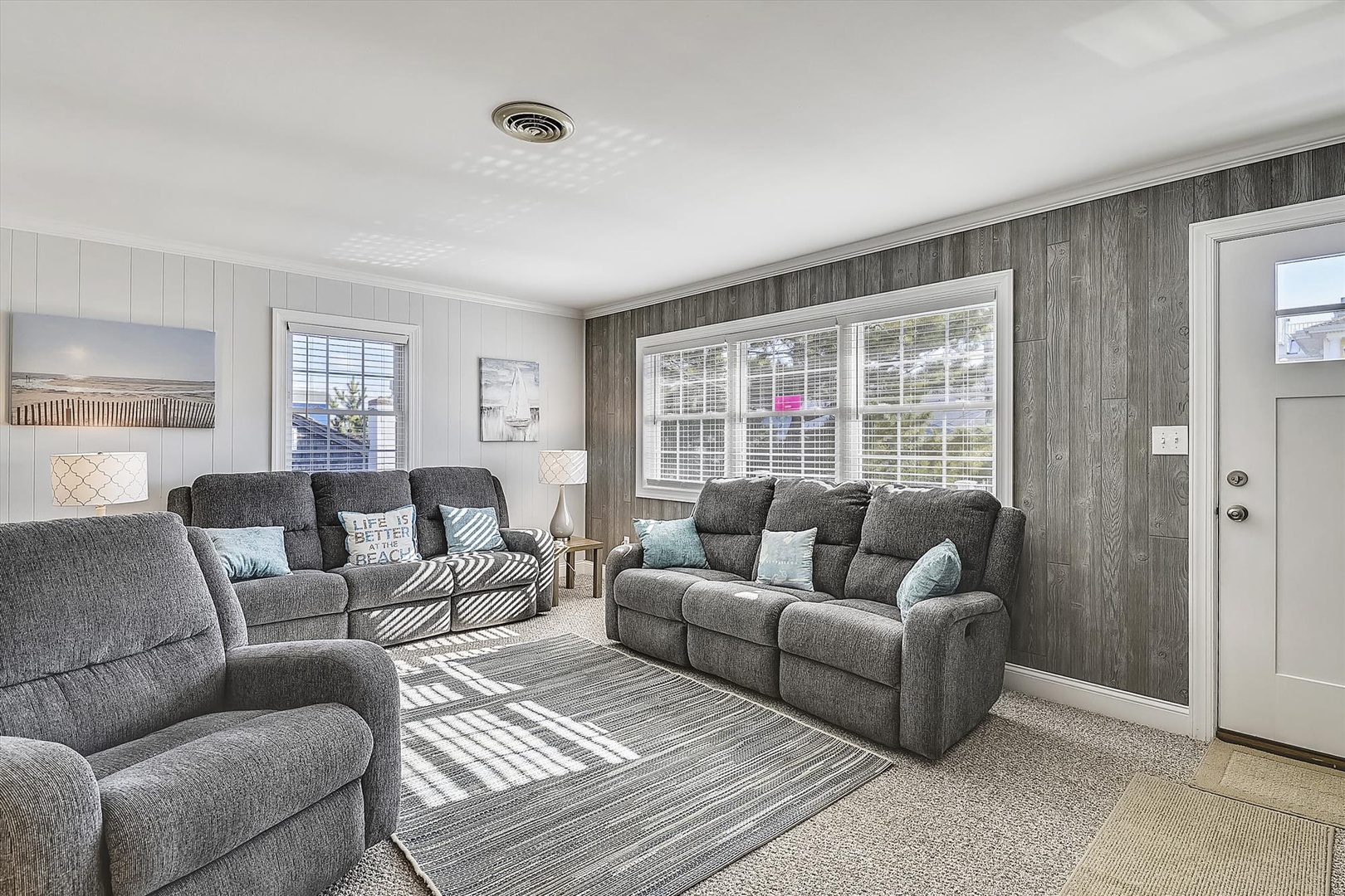 Sink into plush recliners and unwind in your sunlit living room, where coastal charm meets modern comfort. Large windows invite natural light, perfect for peaceful moments together.