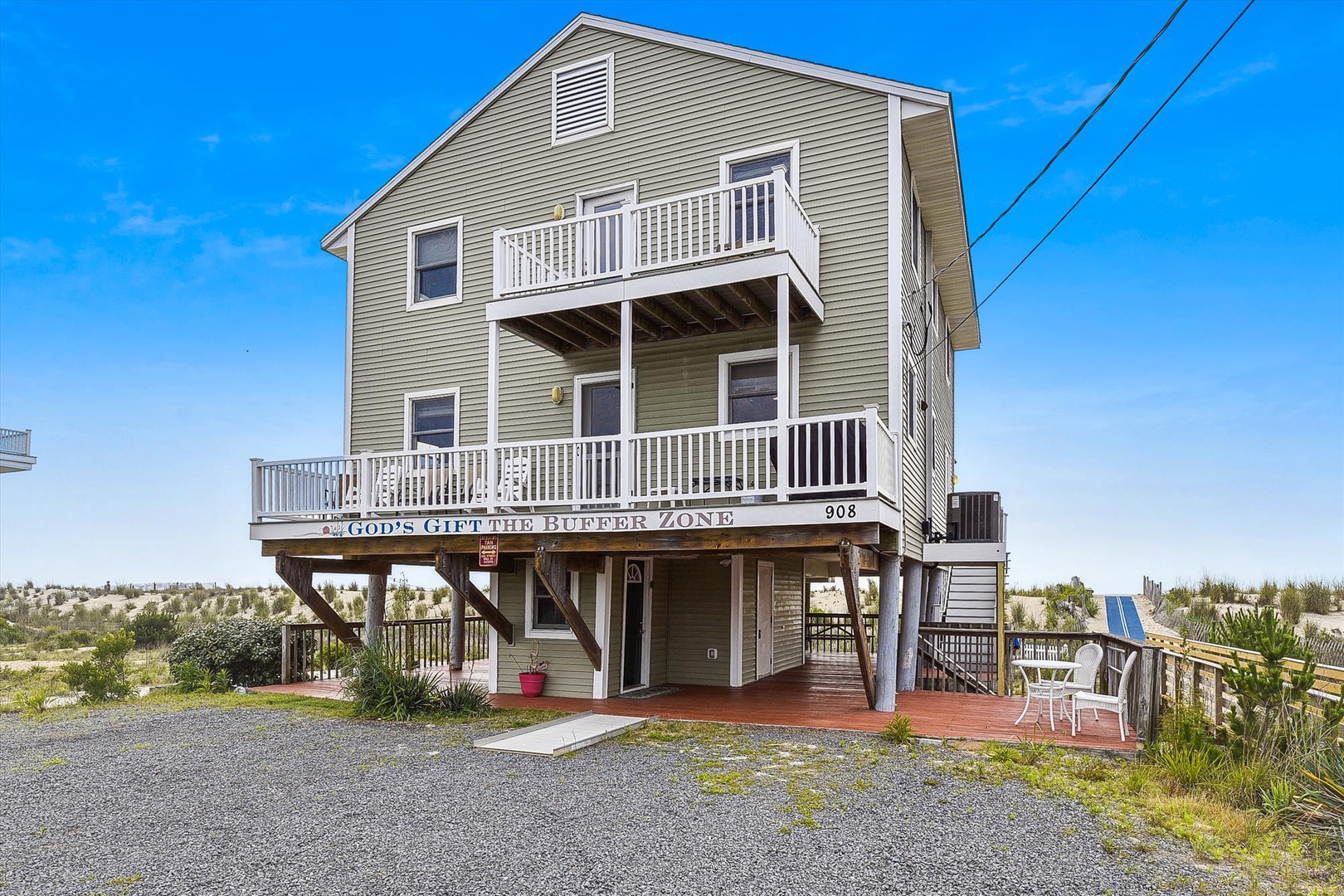 A beachside rental elevated on stilts with wraparound decks, outdoor seating, and dune vegetation, located steps from the shoreline in a coastal community.